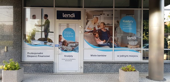 Fasada biura firmy finansowej z naklejonymi na szybach reklamami usług finansowych, w tym kredytów, z logo firmy 'lendi' i hasłami reklamowymi, oraz donicami z zielenią po bokach wejścia.