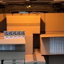 Trasbus - Kartonowe pudła i paczki papierosów w przestrzeni ładunkowej busa. Widok z wnętrza pojazdu, ciemne tło. Transport towarów.