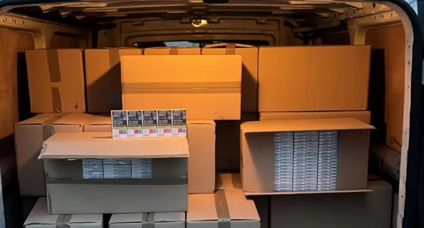 Kartonowe pudła i paczki papierosów w przestrzeni ładunkowej busa. Widok z wnętrza pojazdu, ciemne tło. Transport towarów.