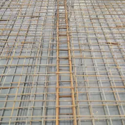 Siatka zbrojeniowa ułożona na czarnej folii hydroizolacyjnej, przygotowana do zalania betonem pod fundamenty.