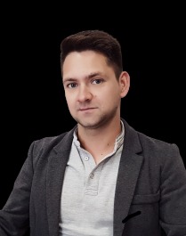 Portret mężczyzny w szarej marynarce i jasnej koszulce polo na czarnym tle.