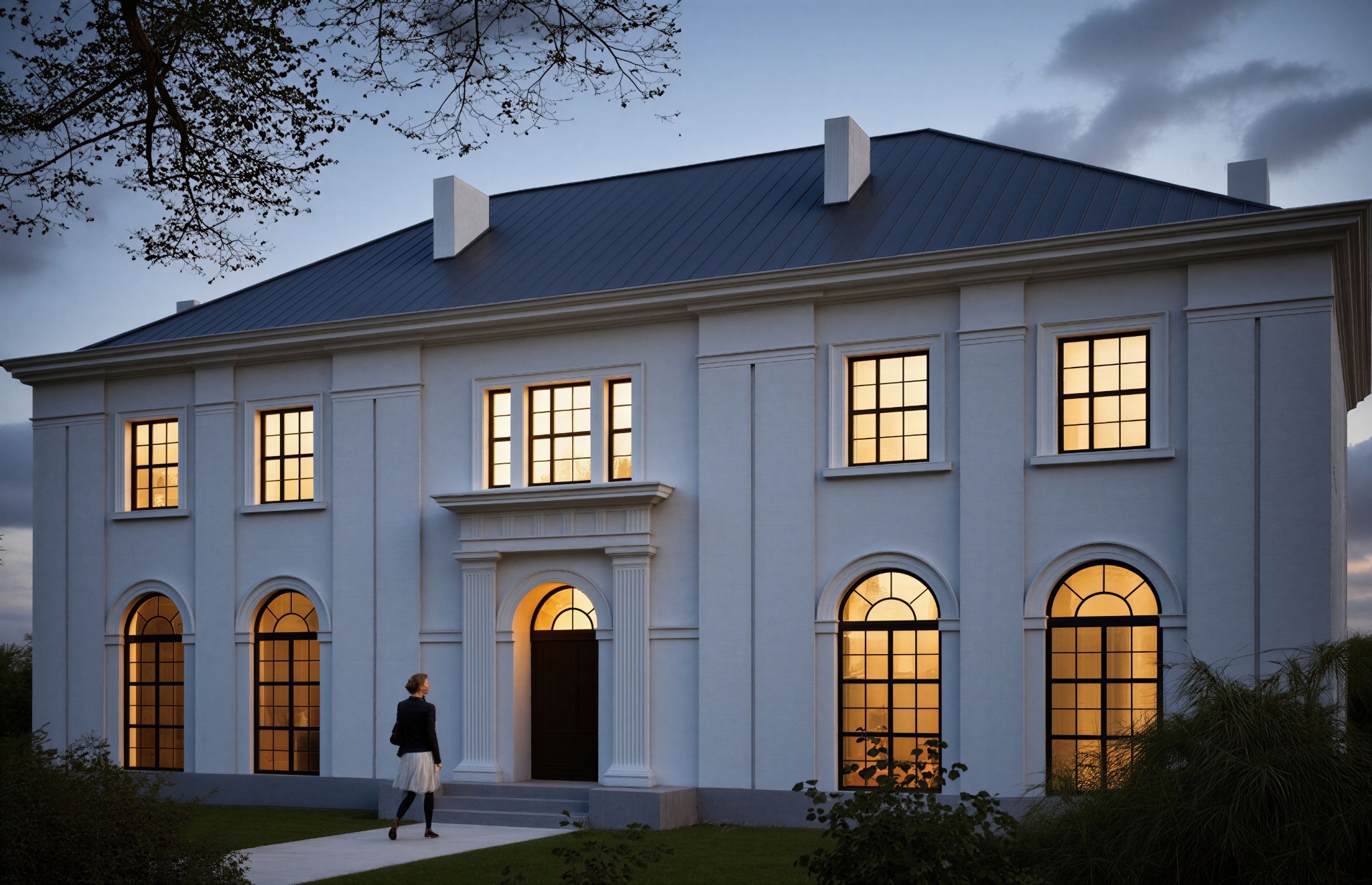 Elewacja dwukondygnacyjnego budynku z symetrycznym układem okien i centralnie umieszczonym wejściem, oświetlona ciepłym światłem wieczornym, z osobą wchodzącą do środka.