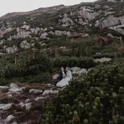 Para młoda siedzi na kamieniach w górskim krajobrazie, w tle skaliste zbocze porośnięte kosodrzewiną.