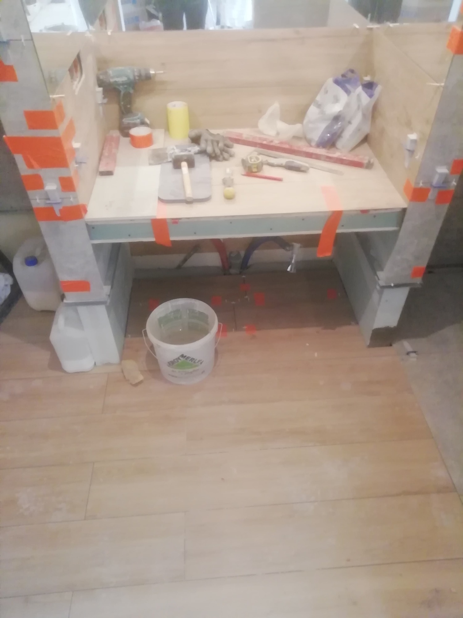 Przygotowania do remontu łazienki: konstrukcja z płyt karton gips, narzędzia, poziomica, wiadro z klejem, wiertarka i zapas płytek na podłodze.