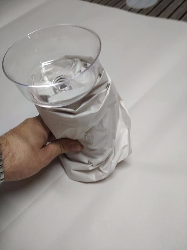 Delikatny szklany kielich zapakowany w biały papier ochronny, trzymany w dłoni, gotowy do transportu.