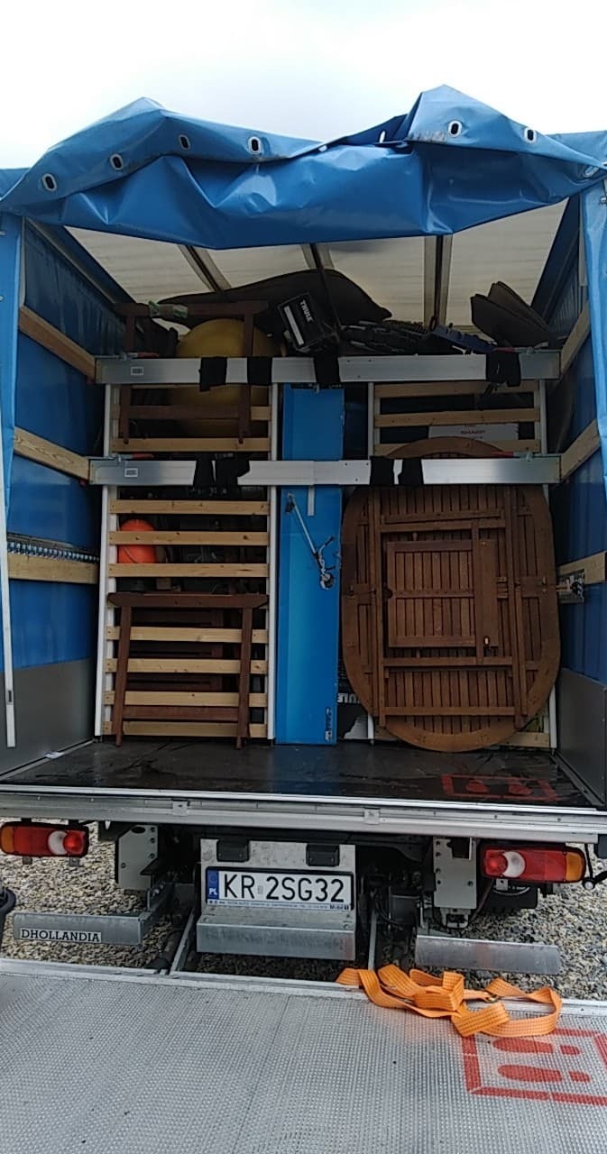 Wnętrze busa z plandeką wypełnione meblami i przedmiotami podczas transportu w Krakowie. Widoczne złożone krzesła, stół i inne przedmioty zabezpieczone wewnątrz pojazdu.