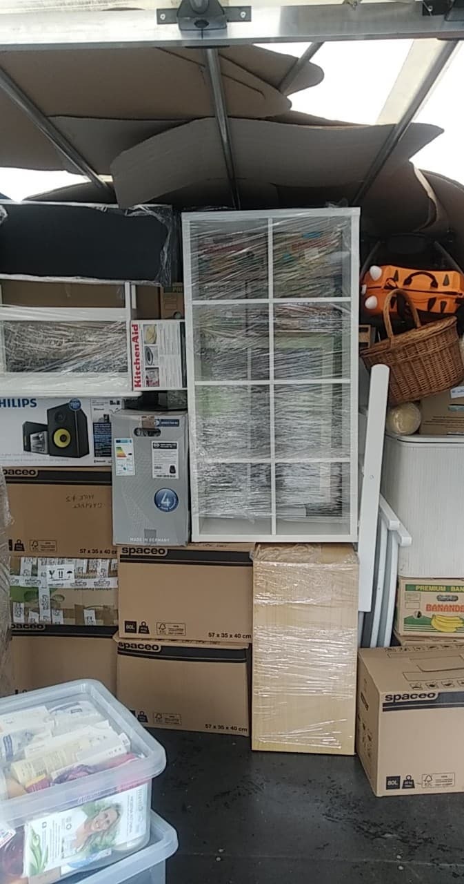 Wnętrze busa wypełnione meblami i kartonami zabezpieczonymi folią stretch, widoczne m.in. regał, sprzęt AGD w oryginalnych opakowaniach oraz pudła z oznaczeniami Spaceo.