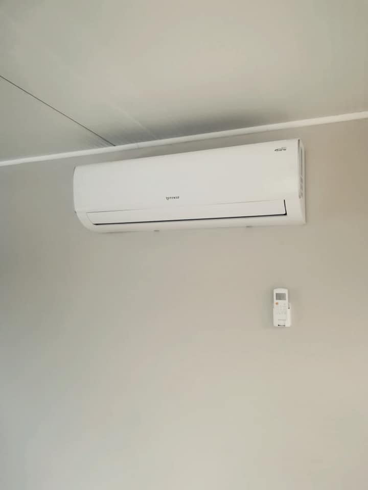 Biały klimatyzator ścienny z pilotem zamontowany na jasnej ścianie w pomieszczeniu.