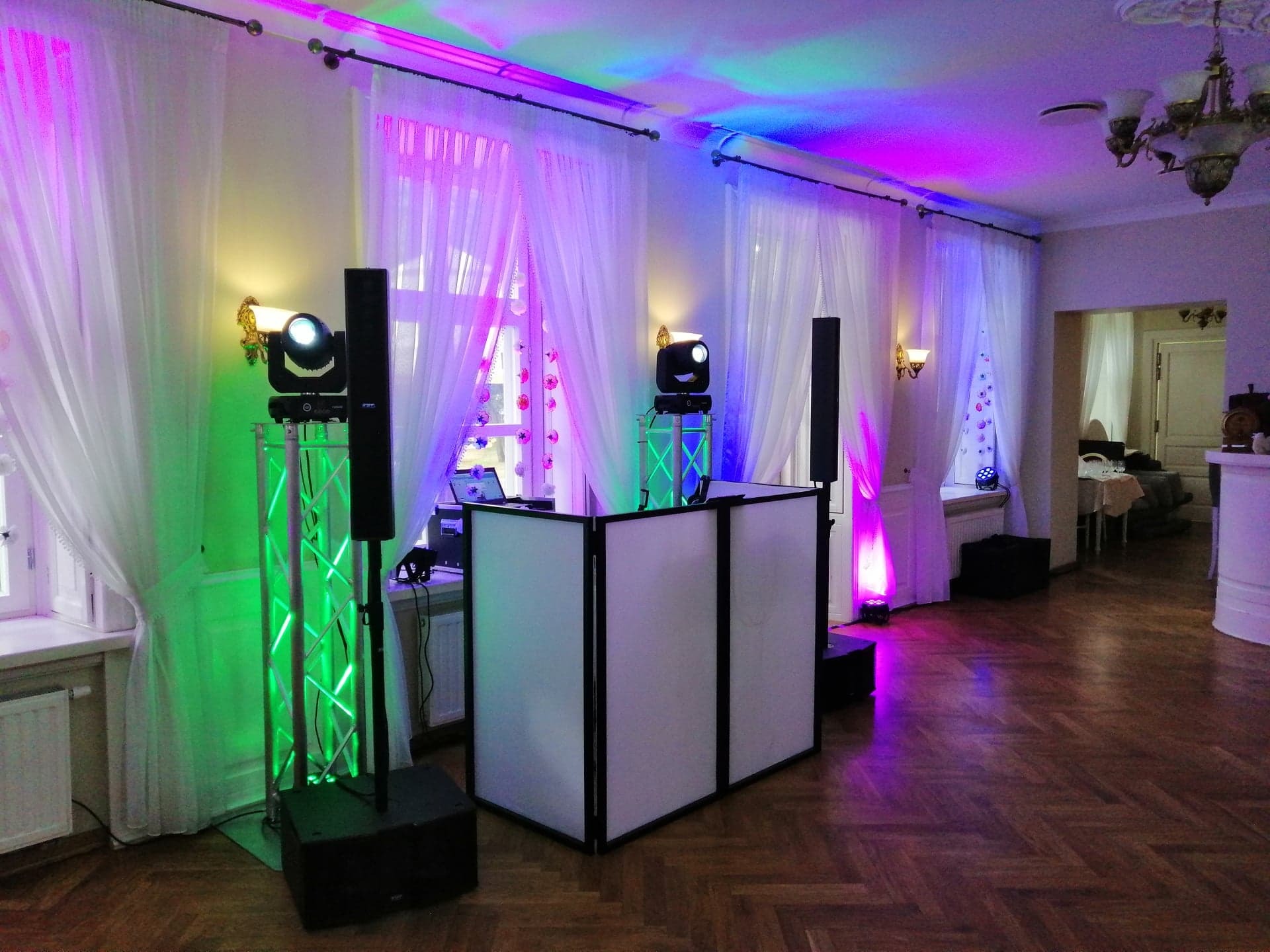 Sala balowa z parkietem, oświetlona kolorowymi światłami, z widocznym stanowiskiem DJ-a, kolumnami głośnikowymi i reflektorami na statywach.