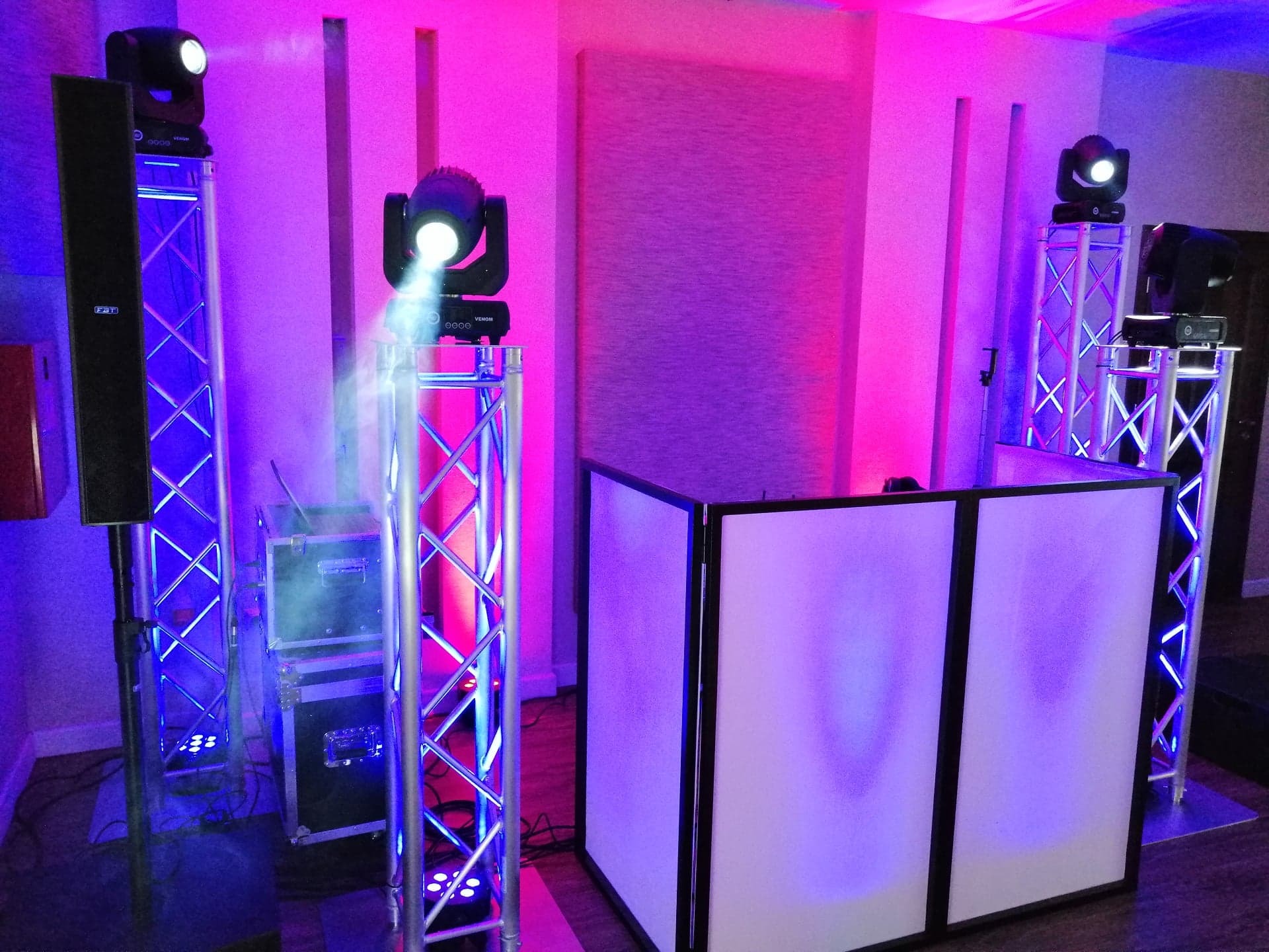 Profesjonalne oświetlenie sceniczne i nagłośnienie z efektami dymu, ustawione na metalowych konstrukcjach, podświetlone na fioletowo i różowo, z widocznym panelem DJ-skim z przodu.