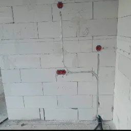 Instalacja elektryczna wewnątrz budynku w trakcie montażu, widoczne puszki instalacyjne i przewody na ścianie z białego bloczka, z napisami oł&oacute;wkiem.