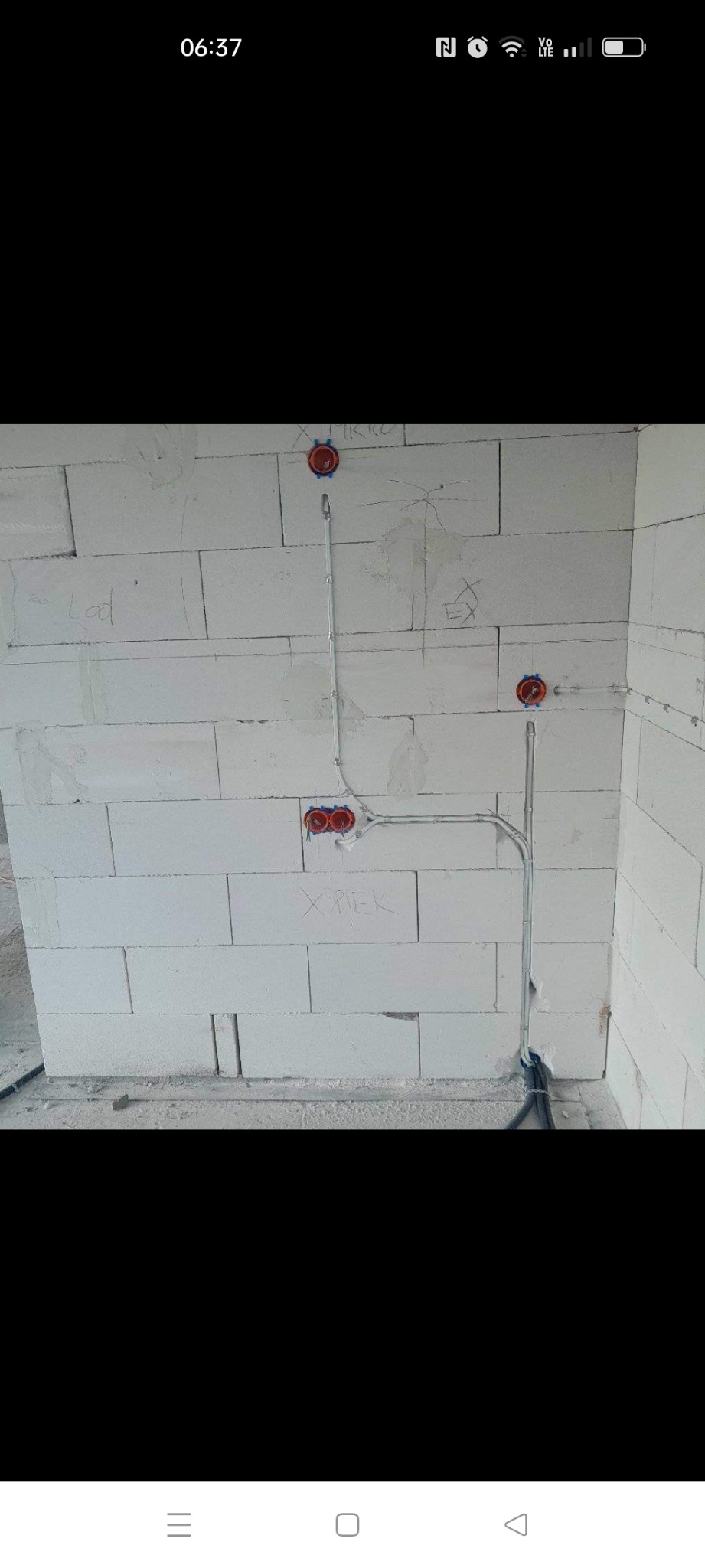 Instalacja elektryczna wewnątrz budynku w trakcie montażu, widoczne puszki instalacyjne i przewody na ścianie z białego bloczka, z napisami ołówkiem.