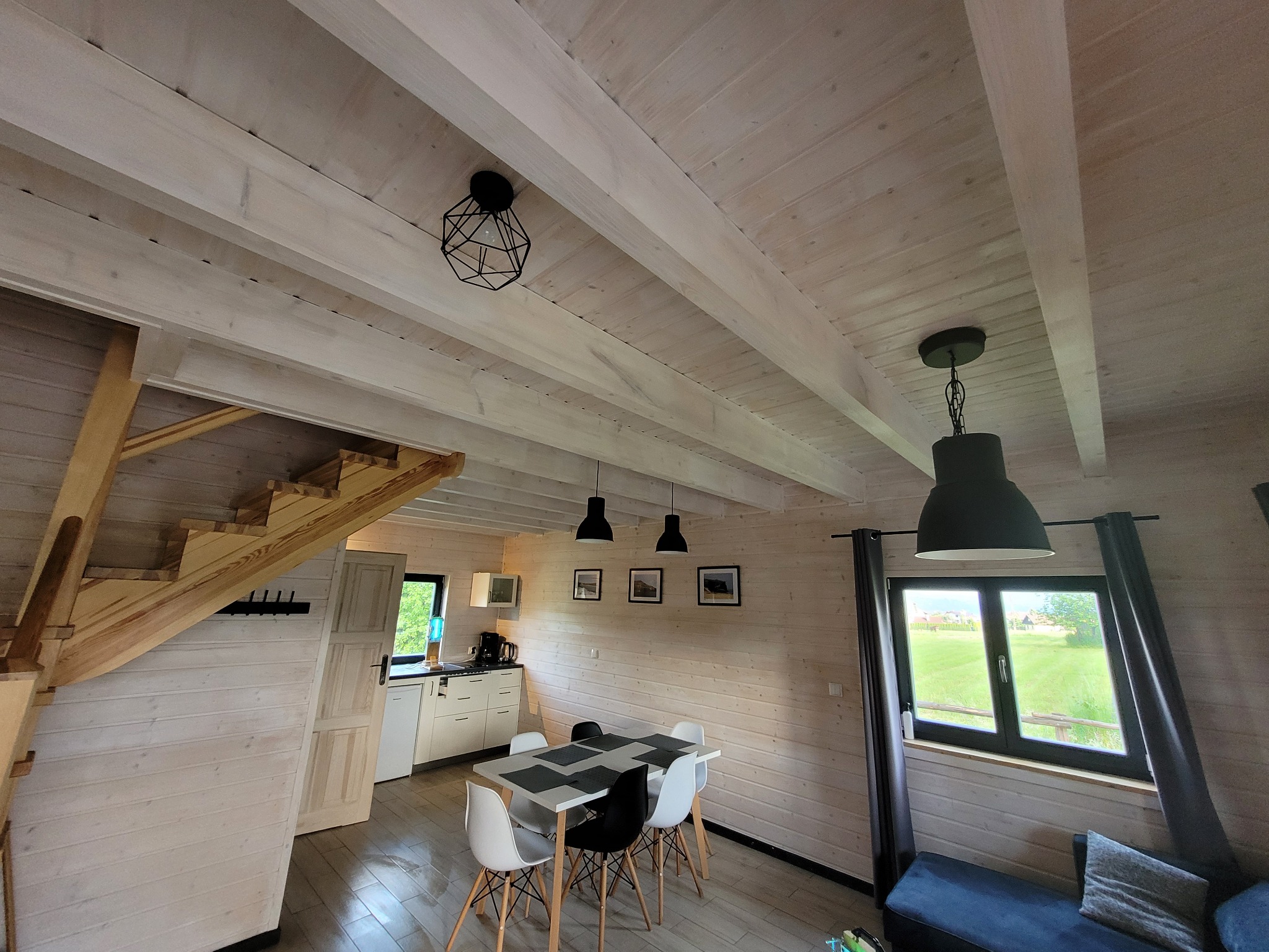 Jasne wnętrze drewnianego domu w Leśnej z widoczną jadalnią, schodami i oknem na zewnątrz, utrzymane w minimalistycznym stylu.