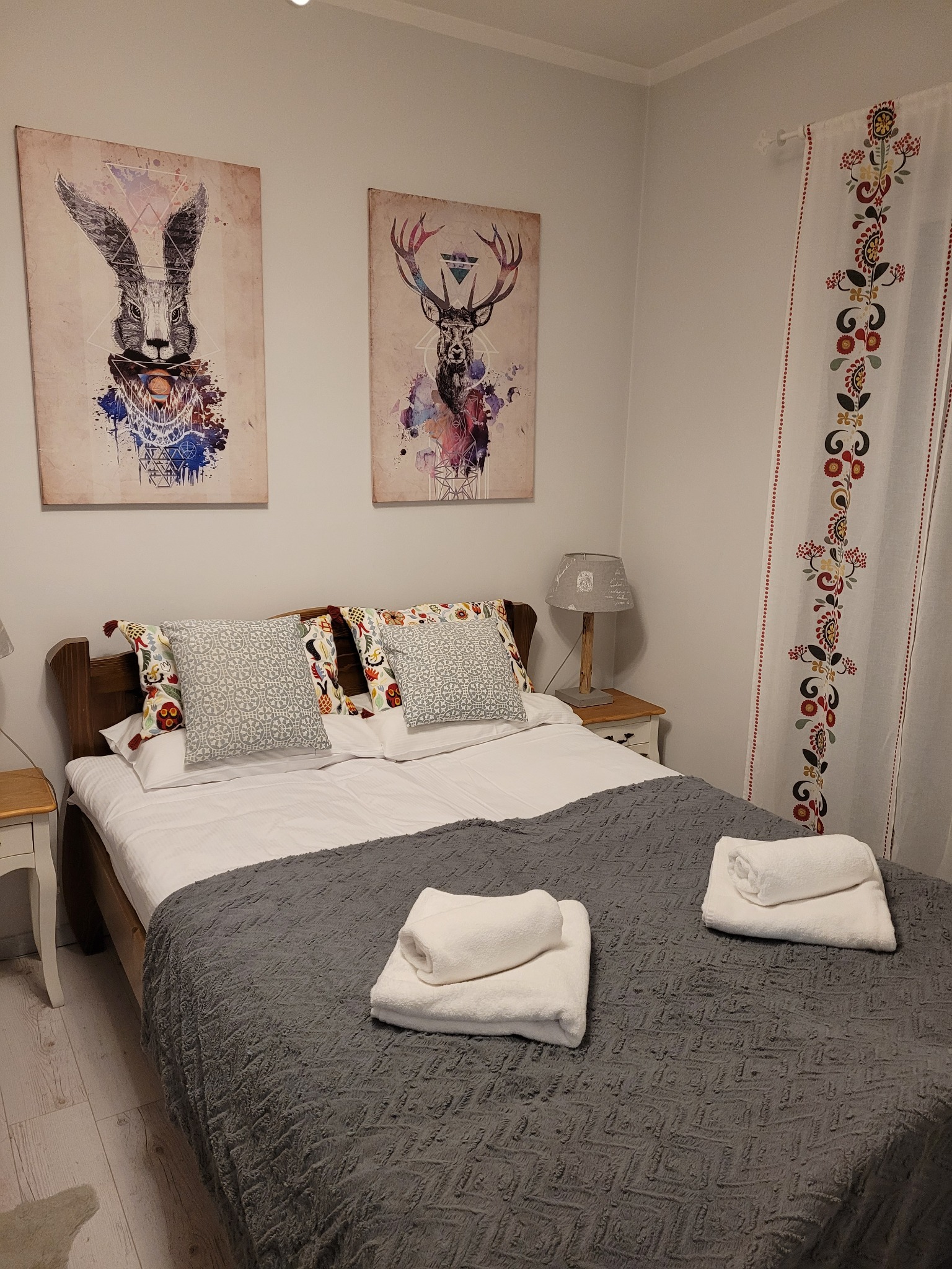 Dwuosobowe łóżko z szarą narzutą i białymi ręcznikami w sypialni z dekoracjami ściennymi w stylu boho.