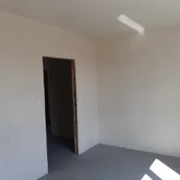 Wnętrze pokoju po szpachlowaniu i gładziowaniu ścian, widoczny otwór drzwiowy z surowym obramowaniem oraz plama światła na ścianie.