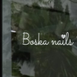 Zalogowana - Elegancki napis 'Boska nails' w kolorze białym, umieszczony na szklanej witrynie salonu, z widocznym odbiciem zieleni w tle.