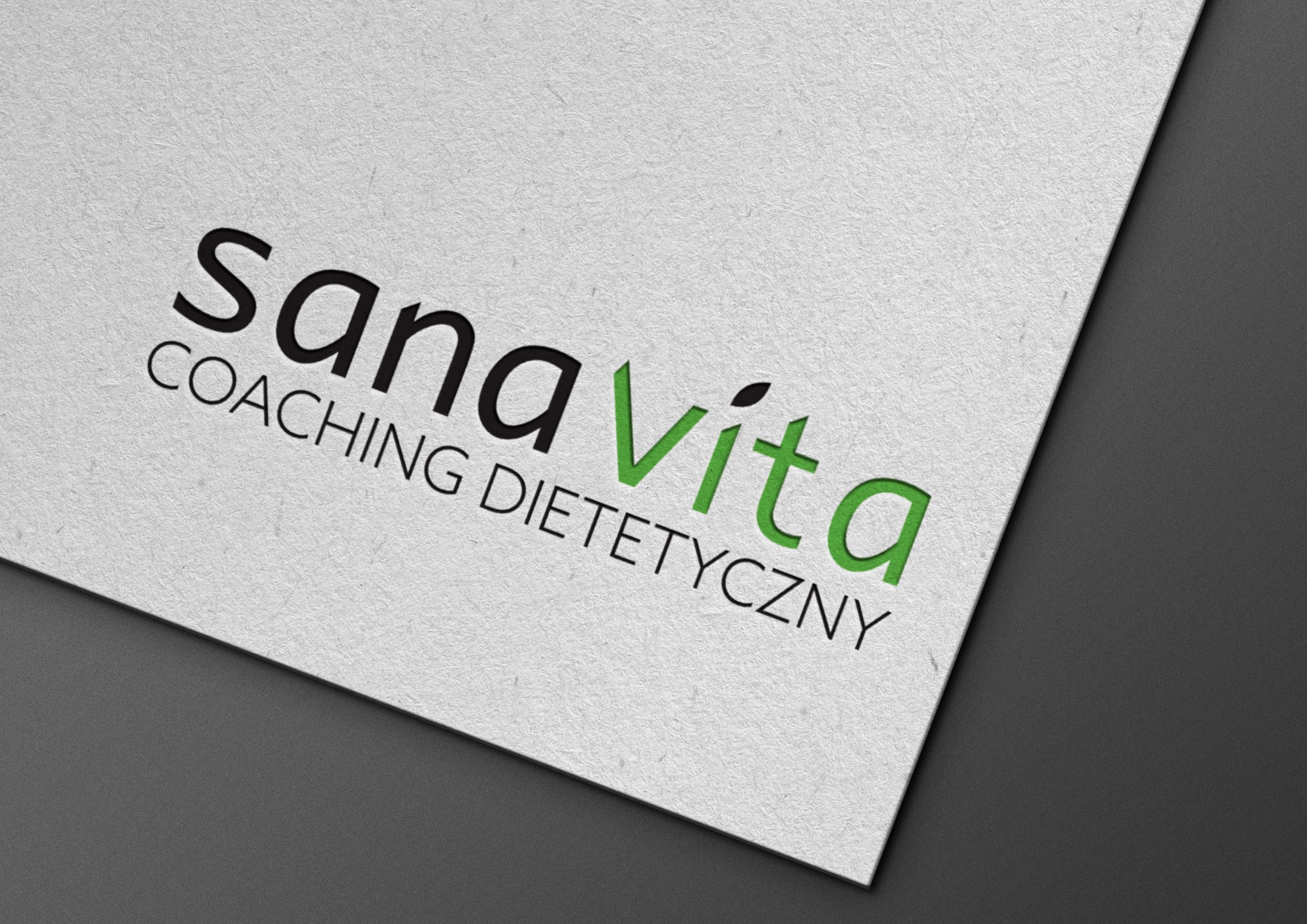 Logo 'Sana Vita Coaching Dietetyczny' w czcionce bezszeryfowej, z zielonym napisem 'Vita' zakończonym małym listkiem, umieszczone na teksturowanym białym papierze pod kątem.