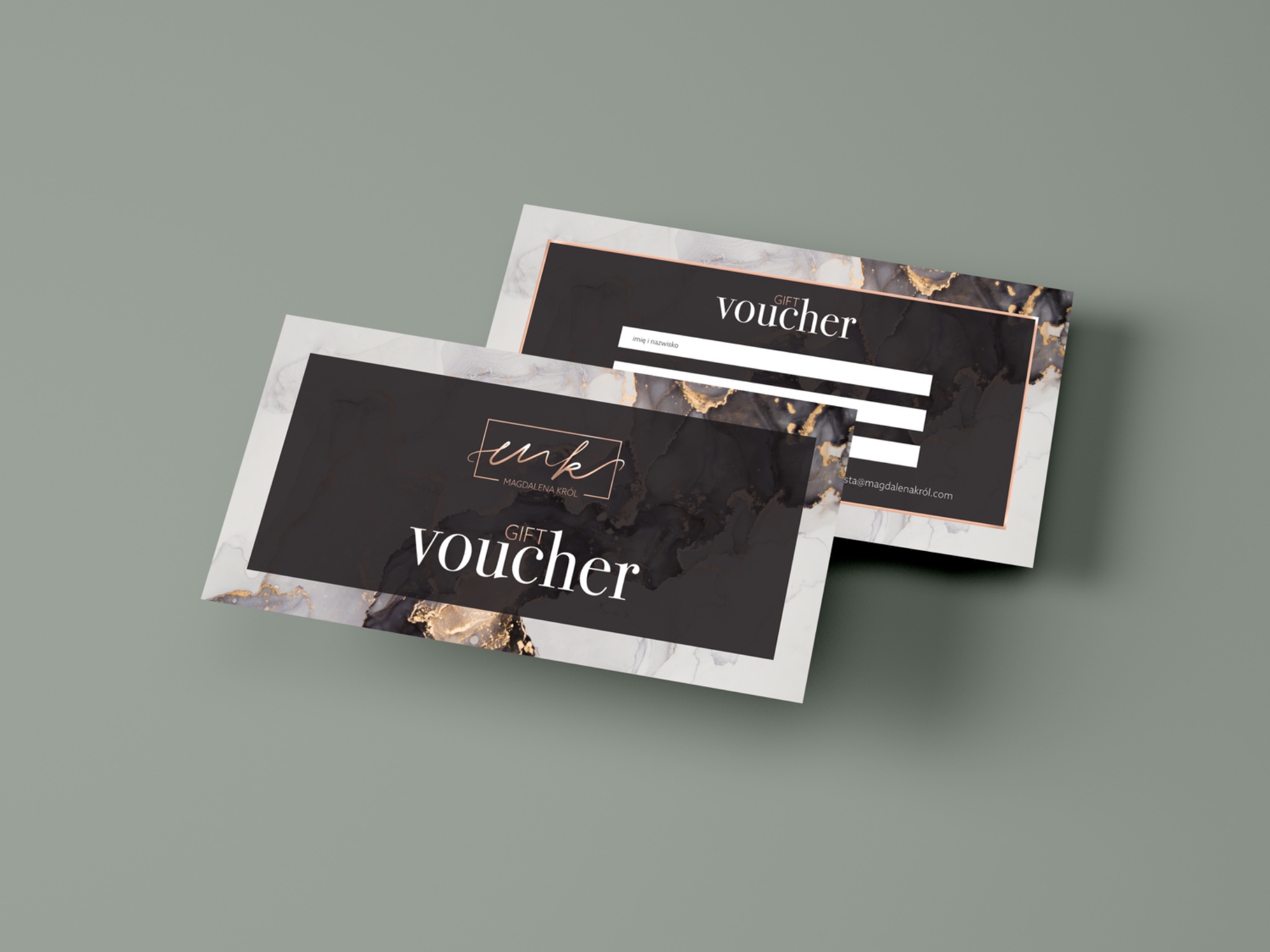 Dwa eleganckie, czarno-białe vouchery prezentowe z motywem marmuru i złotych akcentów, leżące na szarym tle, z widocznym logo i miejscem na wpisanie imienia i nazwiska.