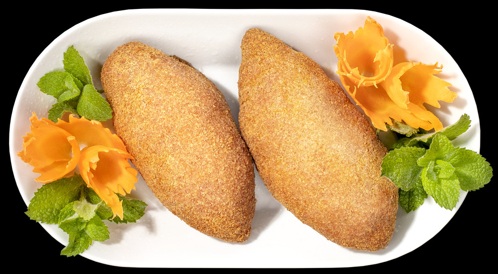 Dwa krokiety z mięsem na białym talerzu, udekorowane listkami mięty i rzeźbioną marchewką w kształcie kwiatów, na czarnym tle.