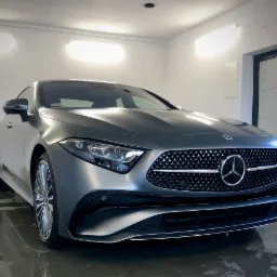 Szary Mercedes-Benz CLS po umyciu, widoczne krople wody na lakierze, chromowany grill i felgi, białe oświetlenie garażowe.