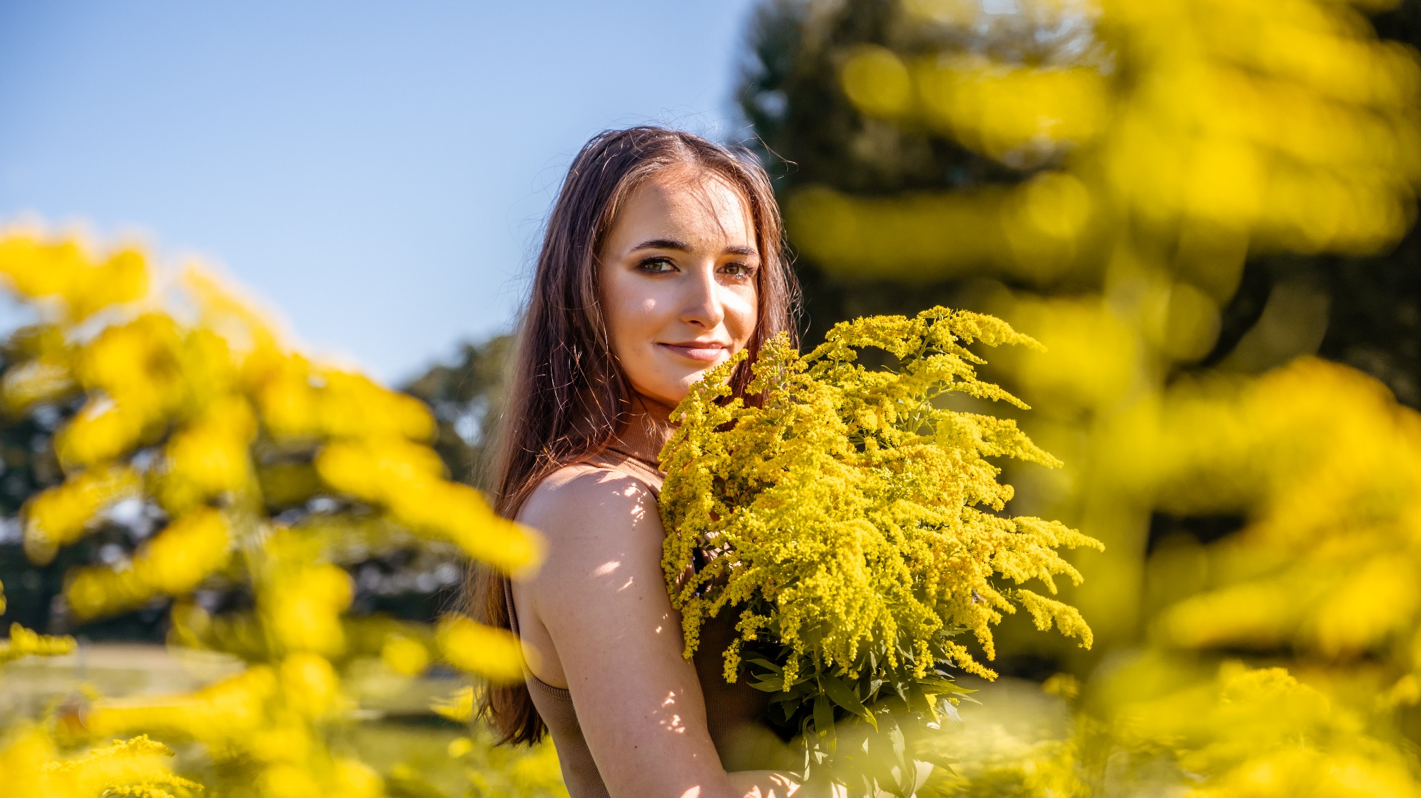 Portret uśmiechniętej kobiety z bukietem żółtych kwiatów na tle słonecznego krajobrazu w okolicach Cholerzyna.