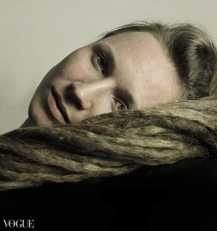 Portret kobiety z długimi, jasnymi włosami, opierającej głowę na włosach, z delikatnym makijażem i spokojnym spojrzeniem.