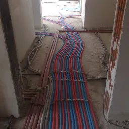 Równolegle ułożone, spięte w regularnych odstępach rury instalacyjne w kolorach czerwonym i niebieskim, prowadzone po surowej podłodze w trakcie budowy.