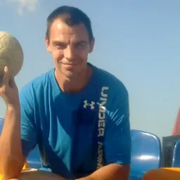 Mężczyzna w niebieskiej koszulce Under Armour siedzi na trybunach stadionu, trzymając w dłoni starą, brudną piłkę do piłki nożnej.