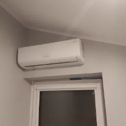 Biała klimatyzacja Rotenso zamontowana nad oknem w jasnym pomieszczeniu, widoczny fragment sufitu i ściany.