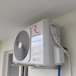 Biała jednostka zewnętrzna klimatyzacji Rotenso Inverter zamontowana na ścianie budynku, widoczne przewody i elementy montażowe.