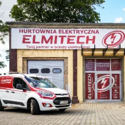 Biały samochód dostawczy z logo 'ELMITECH hurtownia elektryczna' zaparkowany przed budynkiem hurtowni elektrycznej o tej samej nazwie, z widoczną bramą garażową i wejściem z ofertą produktów i usług.