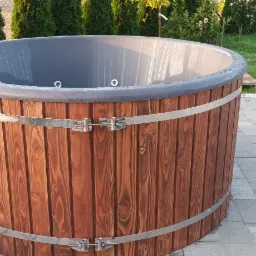 Drewniana balia ogrodowa z szarą wkładką, wzmocniona metalowymi obręczami, na tle kostki brukowej i zieleni.