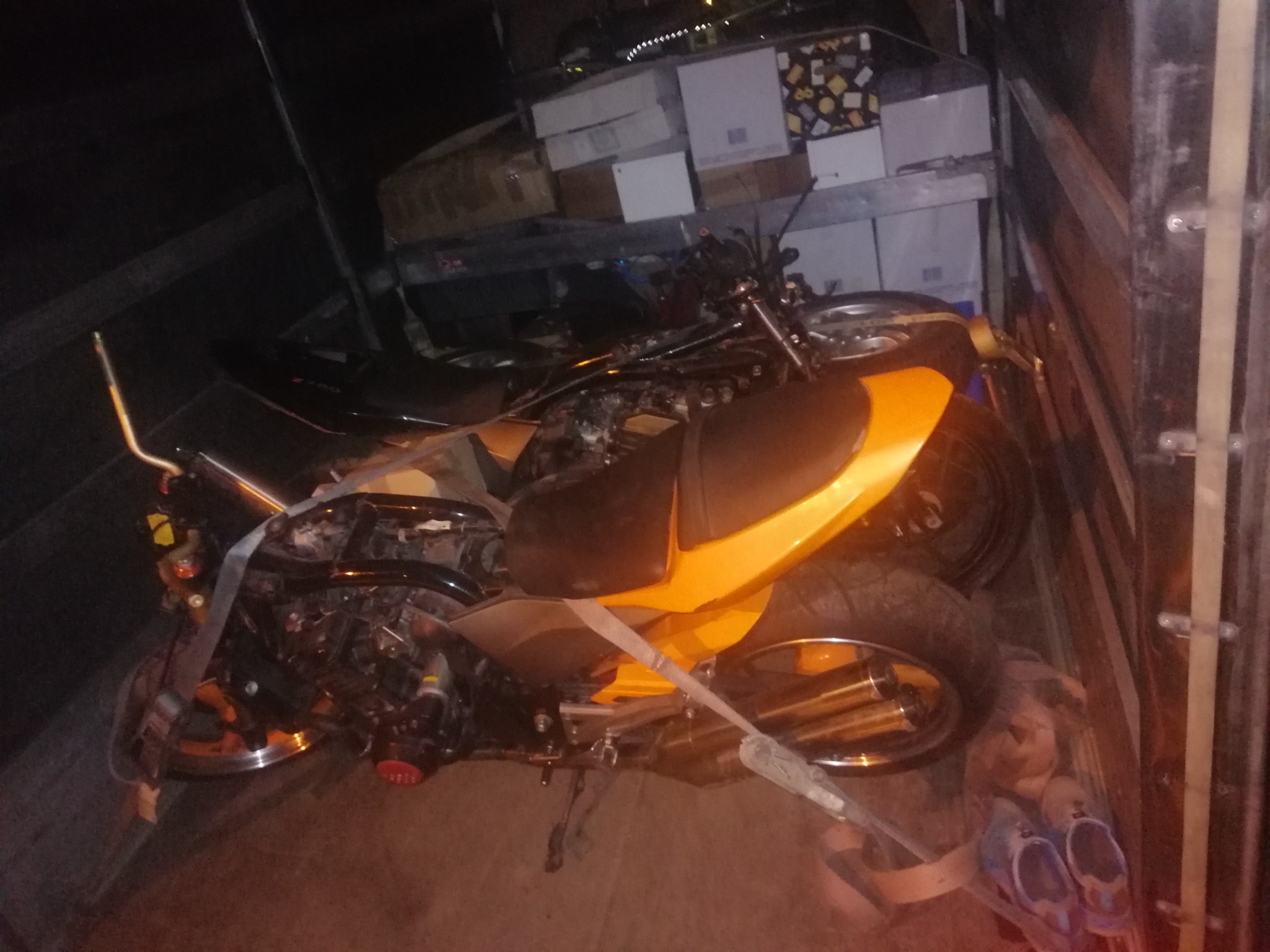 Dwa motocykle zabezpieczone pasami w przestrzeni ładunkowej pojazdu, widoczne kartony i obuwie.