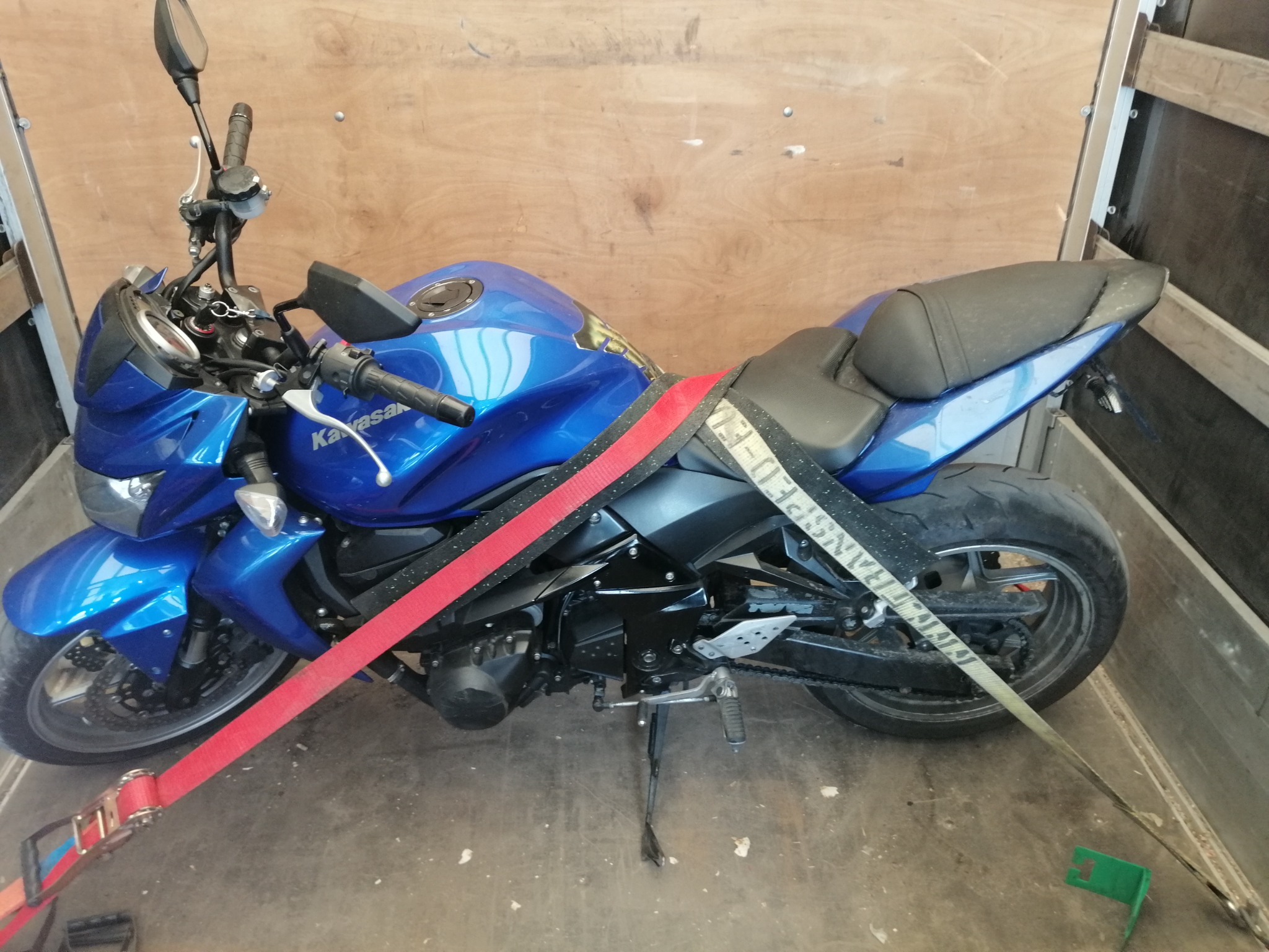 Niebieski motocykl Kawasaki zabezpieczony pasami transportowymi wewnątrz drewnianej skrzyni ładunkowej.