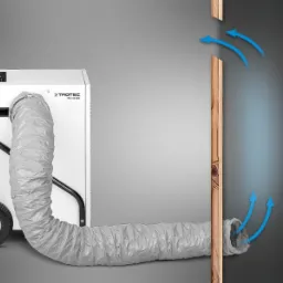 Biały osuszacz kondensacyjny TROTEC TTK 171 ECO z szarym elastycznym wężem podłączonym do otworu w ścianie z cegły, strzałki wskazują obieg powietrza.