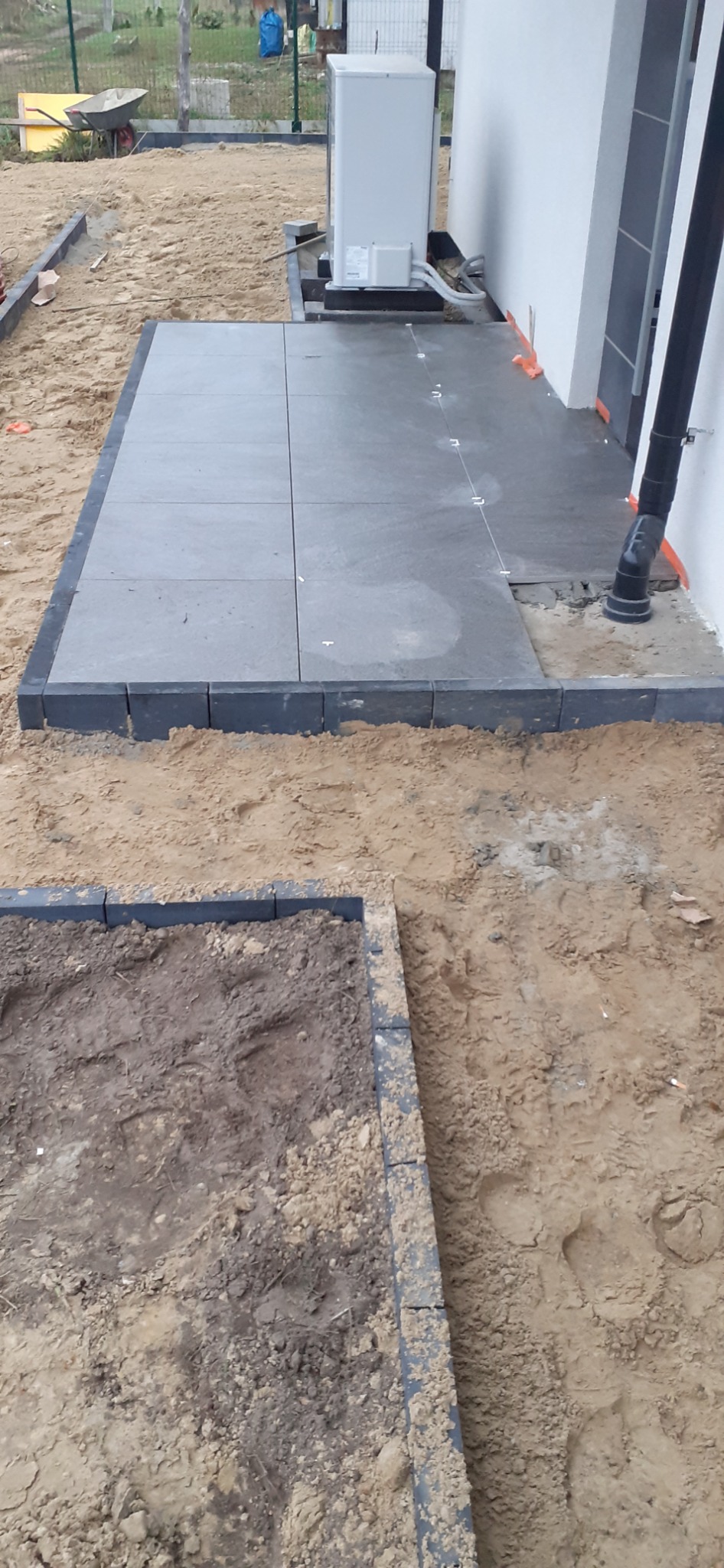 Etap budowy tarasu: ułożone płyty tarasowe i obrzeża z kostki, widoczny piasek i przygotowane podłoże.