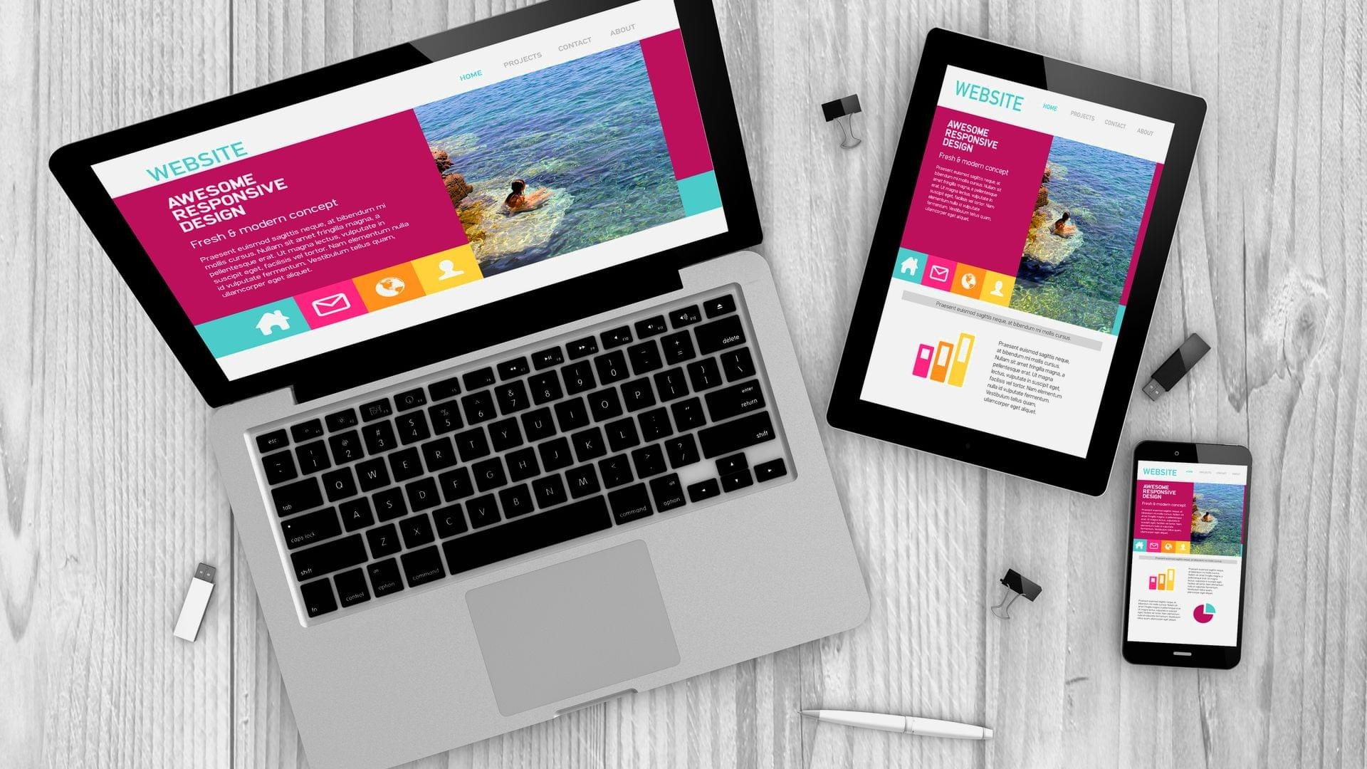 Laptop, tablet i smartfon wyświetlające responsywny projekt strony internetowej z motywem plaży i osoby pływającej w morzu, leżące na drewnianym biurku z akcesoriami biurowymi.