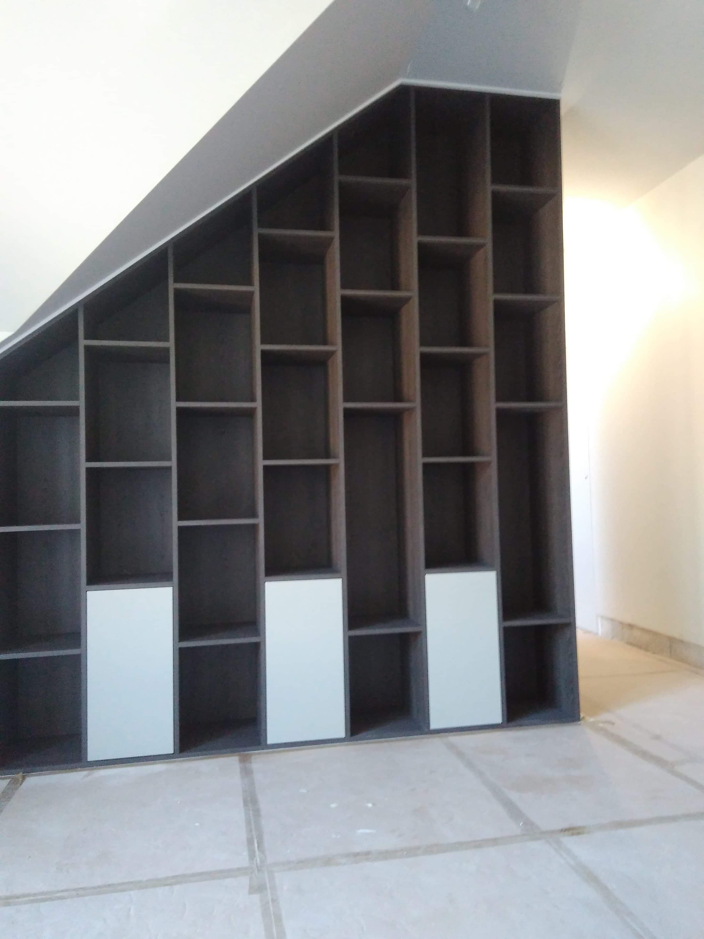 Szara zabudowa regałowa z białymi frontami dopasowana do skosu dachu, widok na puste półki i podłogę w płytkach.