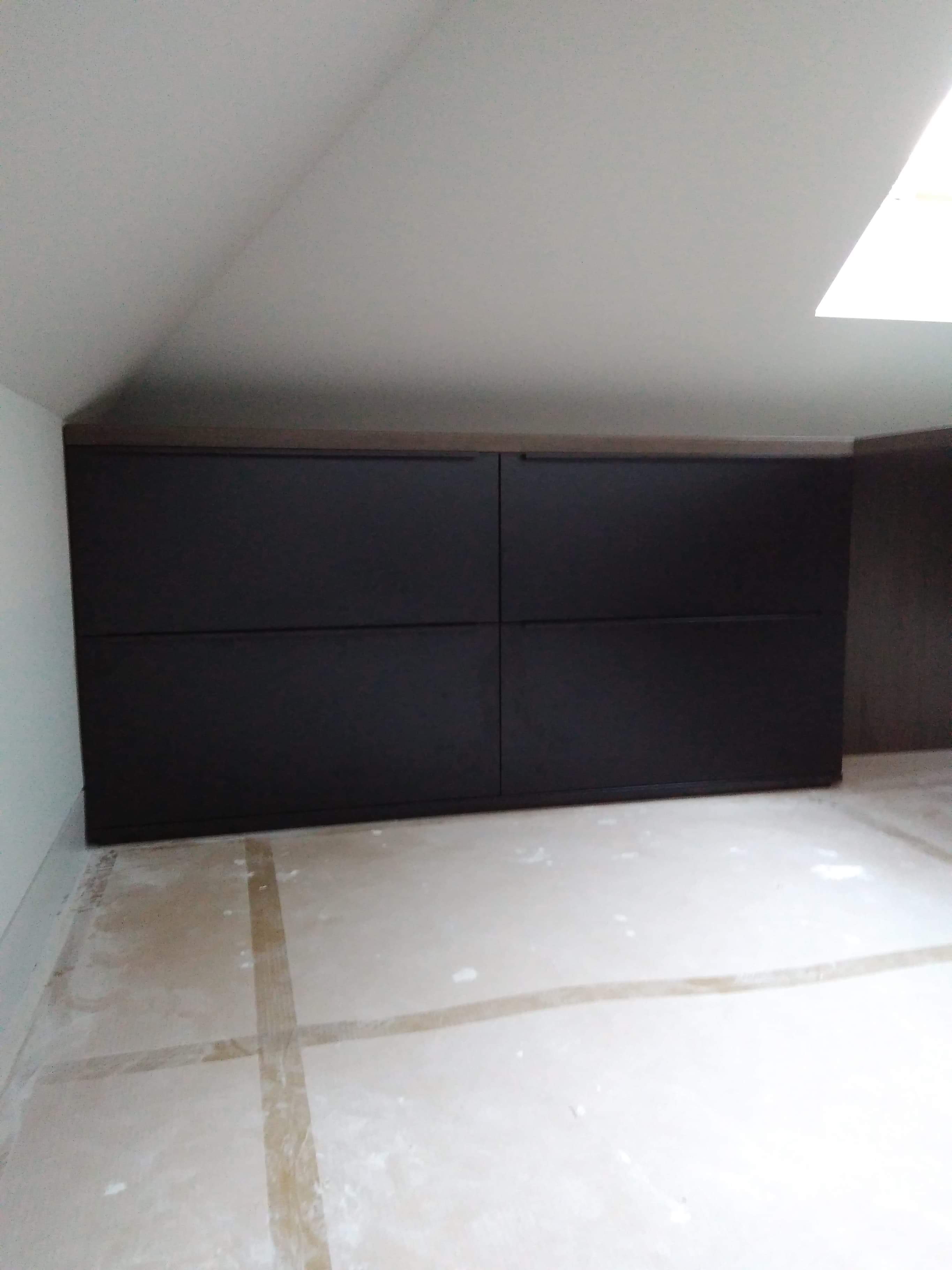 Czarna zabudowa szafy z czterema drzwiami w skosie poddasza, widoczne ślady po malowaniu na podłodze.