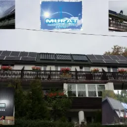 Instalacja paneli słonecznych i kolektorów na dachu budynku z balkonem. Widoczny inwerter i logo firmy. Montaż paneli w toku, z pracownikami na dachu.