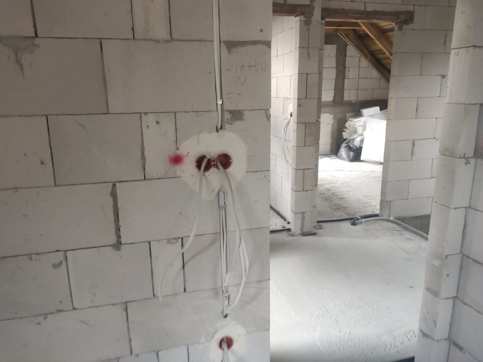 Wewnętrzna ściana z betonu komórkowego w trakcie instalacji elektrycznej; widoczne puszki podtynkowe z wyprowadzonymi przewodami. Surowy stan budynku.