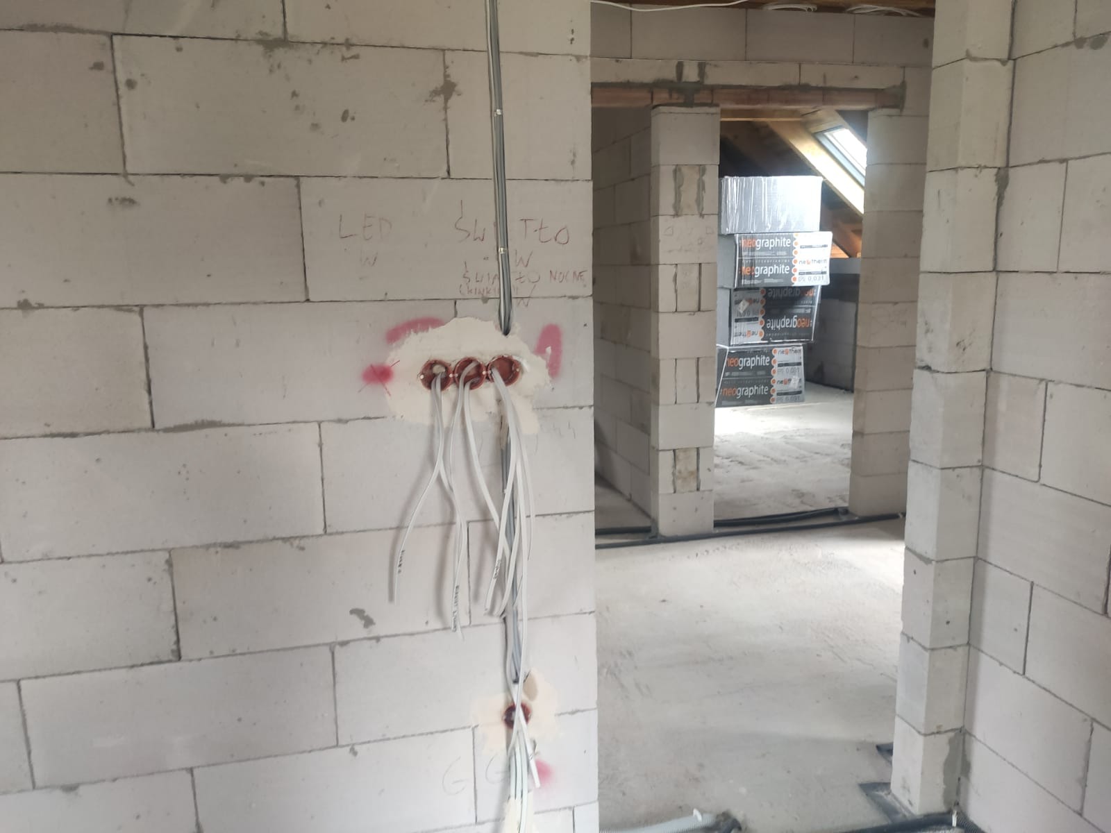 Wewnętrzna instalacja elektryczna w surowym budynku. Widoczne przewody wychodzące ze ściany z betonu komórkowego, z napisem 'LED' i 'Światło'.