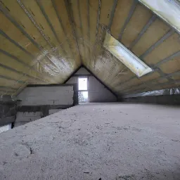 Poddasze z oknem dachowym, ocieplone wełną mineralną i zabezpieczone folią, widoczne metalowe profile mocujące, surowy betonowy strop.