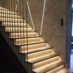 Nowoczesne schody drewniane z podświetleniem LED, metalowa balustrada, ściana wykończona betonem architektonicznym i dekoracyjnym oświetleniem liniowym