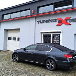 EXTREME DESIGN - Ciemny sedan Lexus GS na tle budynku warsztatu Tuning Xtreme z logo. Widoczne detale: felgi, chromowane listwy, kostka brukowa. Drugi samochód w tle.