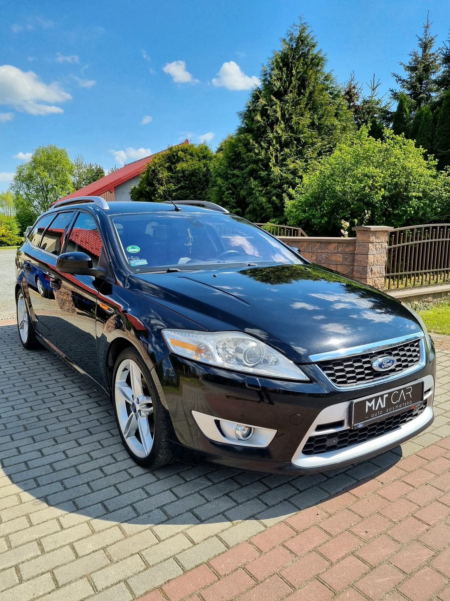 Błyszczący, czarny Ford Mondeo kombi po auto detailingu, zaparkowany na kostce brukowej w słoneczny dzień. Widoczne logo firmy detailingowej.