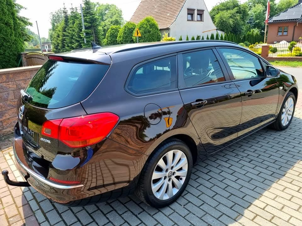 Błyszczący, brązowy samochód kombi, Opel Astra, zaparkowany na brukowanej nawierzchni w słoneczny dzień. Widoczne odbicia w karoserii.