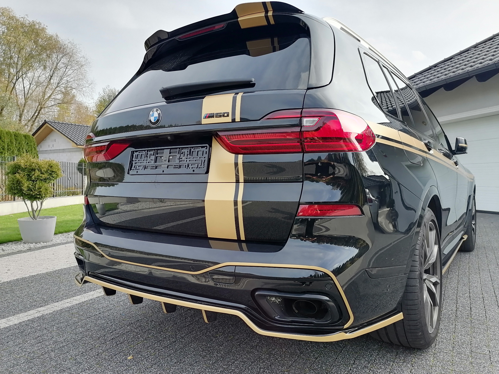 Czarny BMW X5 M50i z złotymi pasami i akcentami, widok z tyłu, tuning wizualny, nowoczesny design.