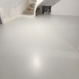 Jasnoszara, gładka posadzka żywiczna w surowym wnętrzu, widoczne schody betonowe w trakcie budowy, instalacja grzewcza na ścianie.