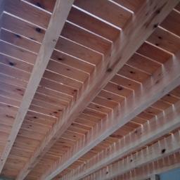 DREW-DOM Adrian Hauf - Drewniana konstrukcja dachu z widocznymi belkami i deskami, jasne drewno z naturalnymi sękami, widok od dołu.